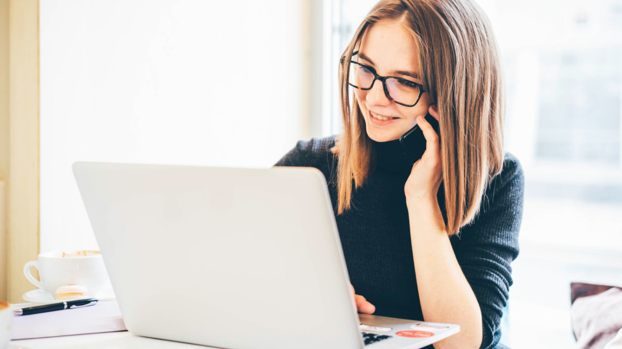 woman checks laptop while talking on cell phone